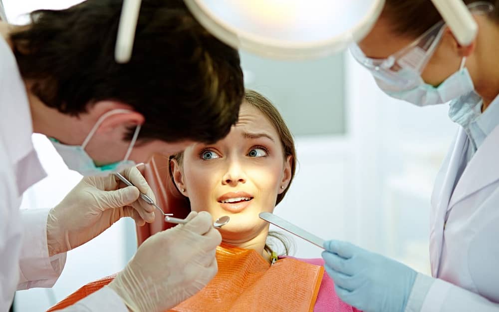 A fearful woman is being examined by a dentist.