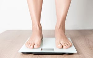 A woman's feet on a weight scale during Invisalign treatment.