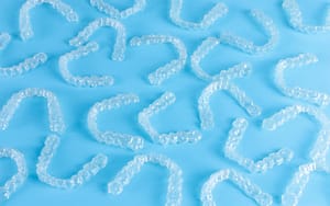 A group of clear plastic Invisalign teeth whitening trays on a blue background.