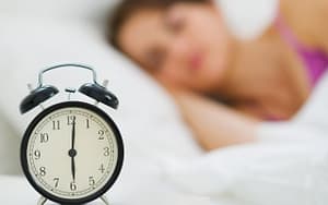 A woman next to an alarm clock in bed seeks tips for her Invisalign® treatment.