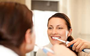 A woman practices oral health by brushing her teeth in front of a mirror.