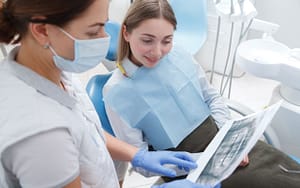 A woman examines a picture while seated in a dentist's chair, possibly related to impacted wisdom teeth.