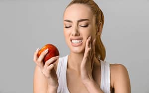 A woman finding relief from a toothache with a home remedy, closing her eyes while holding an apple.