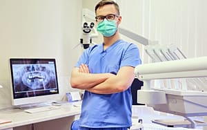 A dental hygienist wearing a surgical mask performing preventative care on a patient in front of a computer.