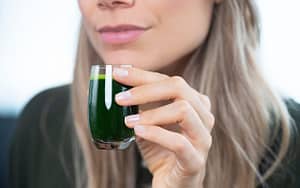 A woman is holding a glass of green juice, which serves as an effective home remedy for toothaches.