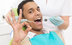 A man in a dentist's chair giving a thumbs up sign after having a knocked-out tooth fixed.
