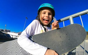 A young girl showcasing oral sports protection by smiling with a skateboard.