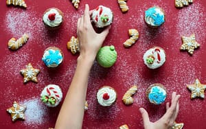 A woman's hand is reaching out to a plate of cupcakes, showcasing delicious Christmas sweets and treats that can harm your teeth.