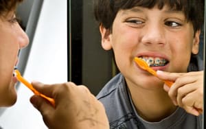 Two pictures of a boy having fun while brushing his teeth with braces.