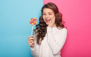 A girl with braces holding a colorful lollipop against a blue and pink background.