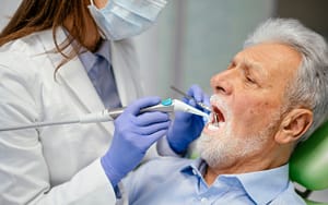An older man is getting his teeth cleaned by a dentist.